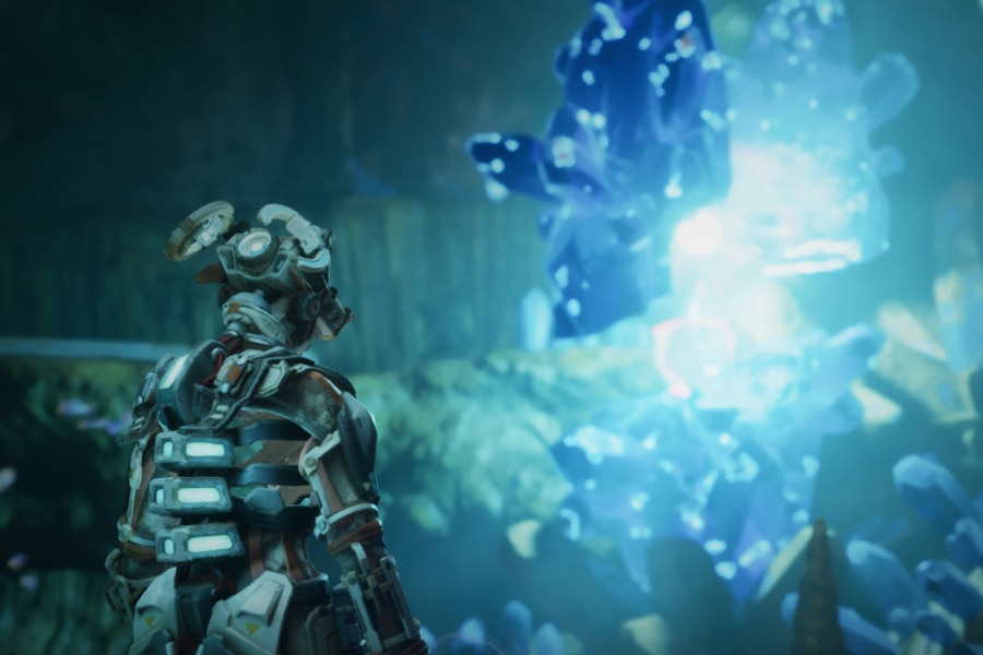 Robot explorer looking toward a bright blue crystal formation in a cavern.
