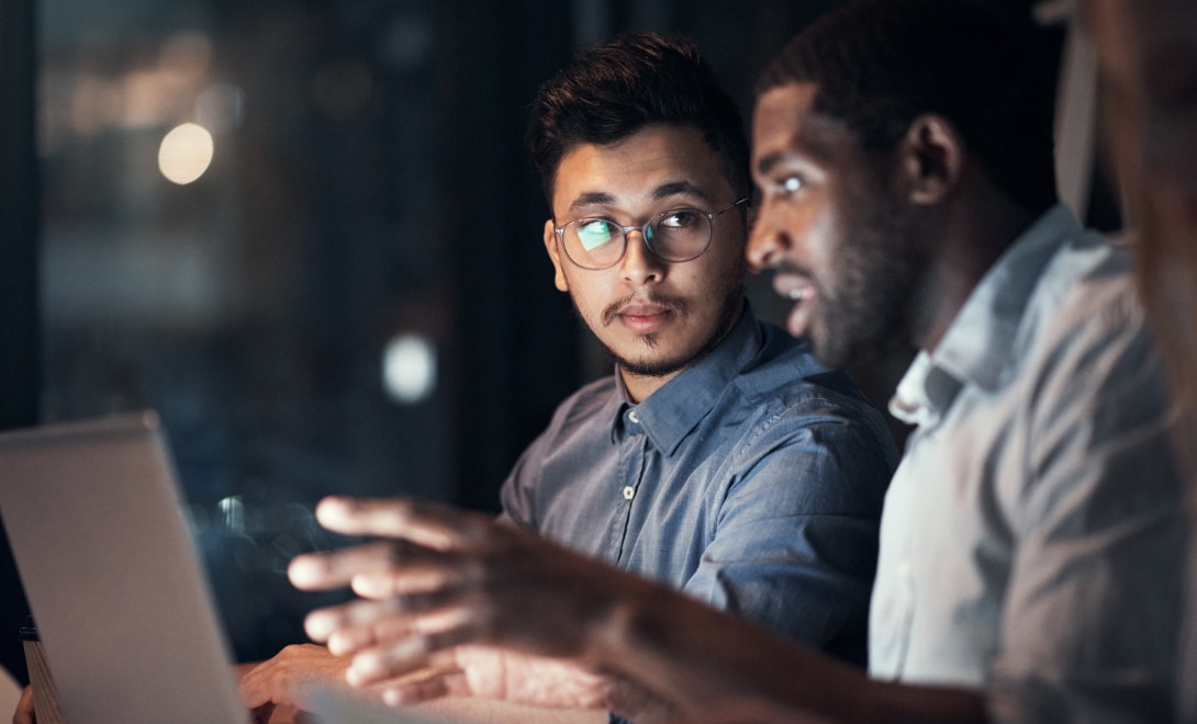 Two software engineers working together on a laptop at night.